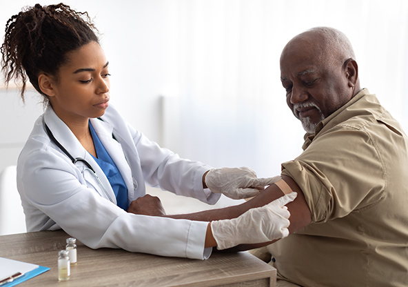 A senior man gets a bandage on his arm after receiving a flu shot from his doctor