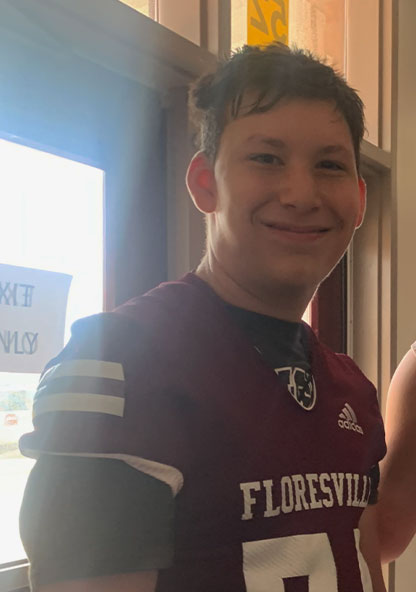 A current picture of Kaden Hickman. He's a teenager and is smiling and wearing a school jersey