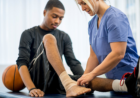 A young basketball player is getting his injured ankle wrapped by a sports medicine specialist