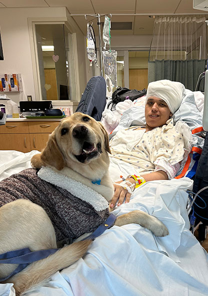 Samuel Trejo smiles with a therapy dog in his bed at CHRISTUS Children's after his epilepsy surgery.