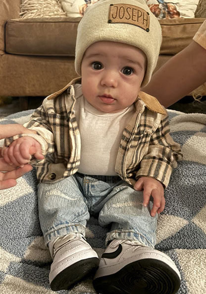 Baby Joseph sitting at home in a beanie hat and a flannel outfit