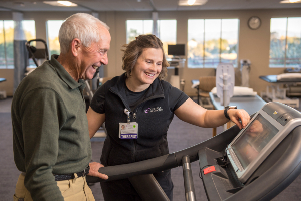 A therapist helping elderly man on a treadmill